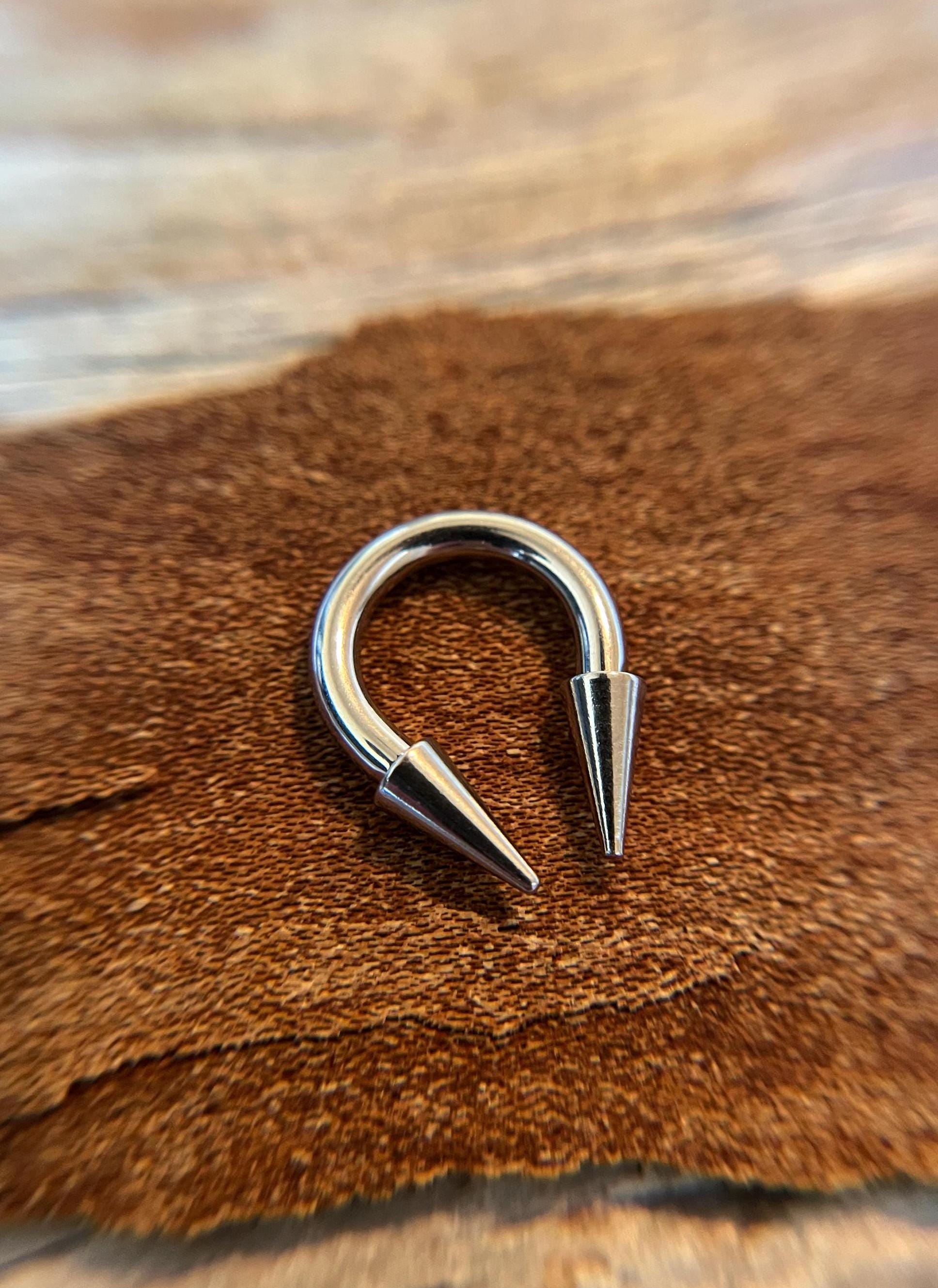 May include: A silver-colored circular barbell with two pointed ends. The barbell is on a brown surface.